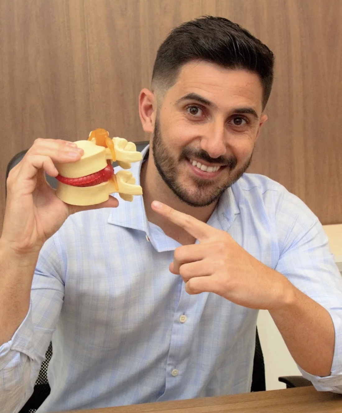 Dr. Jonisson Marques segurando um modelo anatômico de coluna vertebral durante a avaliação